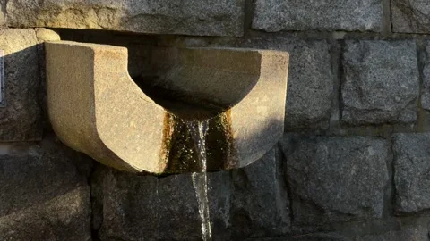 Clear water flows continuously from a carved stone fountain basin set into a Stock Footage 345745568