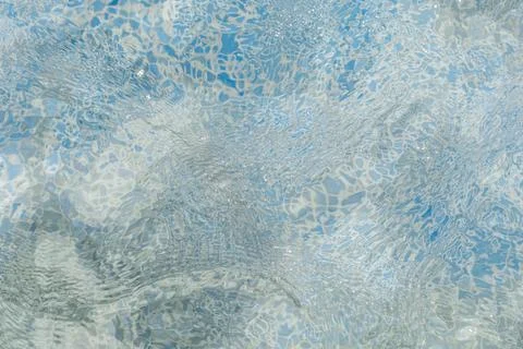Clear water flows gently in a pool, reflecting sunlight and creating patterns Stock Photos