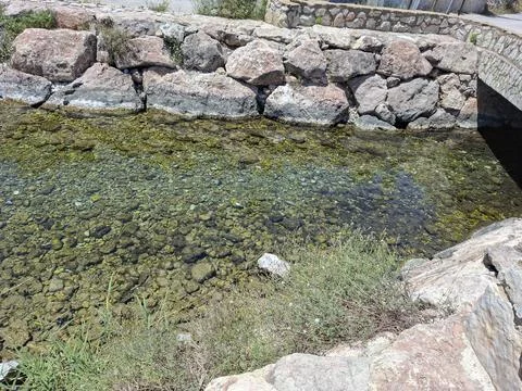 Clear water flows over rocks near stone wall at Font Salada warm spring in .. Stock-Fotos