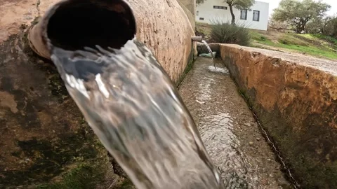 Clear water flows from a weathered pipe embedded in a stone structure Vídeo Stock 331095564