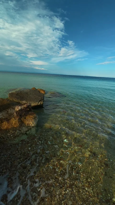 Clear water laps gentle pebbles and weathered rocks. Nikiti, Greece. Vertical Stock Footage 339025521