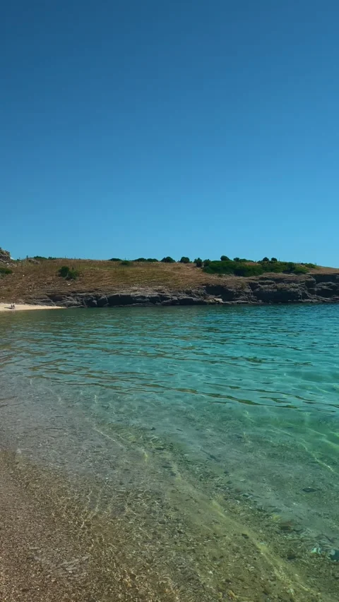 Clear water laps sandy shore under blue sky. Trani Ammouda, Greece. Vertical Stock Footage 339629305