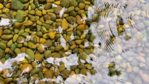 Clear water over a rocky bottom with a reflection of the sky and circles on the  動画素材 341068330