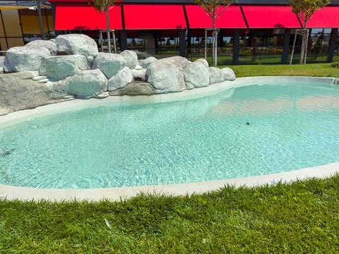 Clear water in a pool surrounded by rocks and grass near a building with re.. Stock Photos