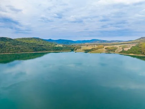 Clear water reflects clouds and hills in a calm body of water surrounded by.. Stock Photos