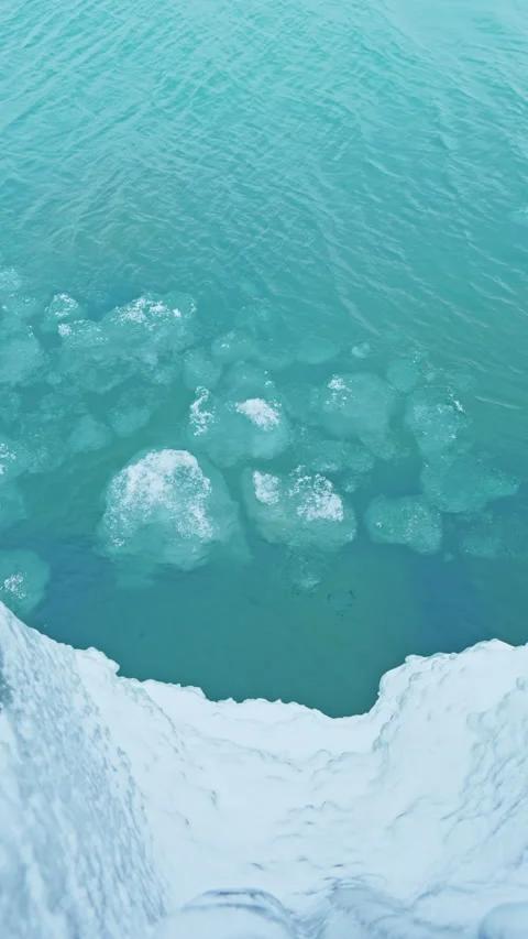 Clear water reveals ice formations under bright sunlight near a cliff edge along Stock Footage 332272104