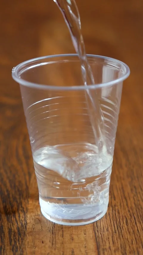 Clear water stream filling empty glass on natural wood background Stock Footage 312358527