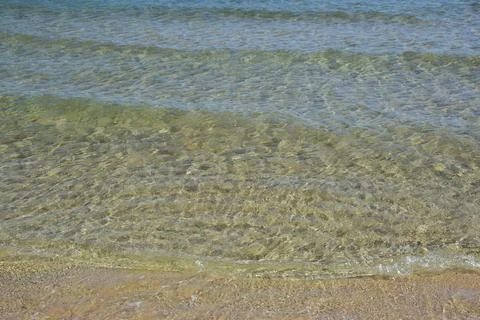 Clear water waves gently lapping on sandy beach shoreline under sunlight Stock Photos