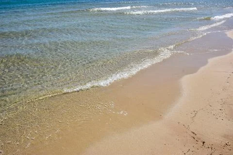 Clear water waves gently lapping on sandy beach under bright sunlight Stock Photos