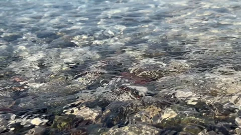 Clear waters waves gently lapping the shoreline, revealing smooth pebbles on a Stock-Footage 273782067