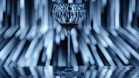 Clear wine glass standing infront of a falling rain like pattern in the Stock Footage 233695182