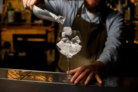 Clear wine goblet glass in which bartender gently pours ice cubes from a scoop 스톡 사진