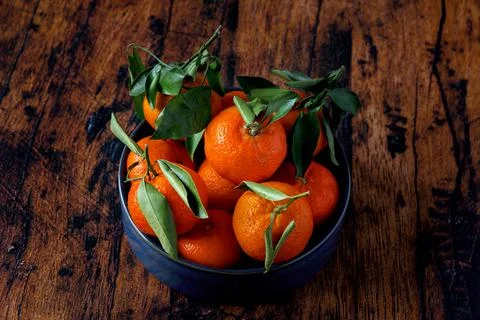 Clementines with leaves in a blue ceramic dish on an old wooden table Foto stock