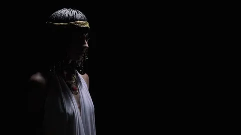 Cleopatra in dramatic lighting is lifting her hands up and looks above Stock Footage 138139983