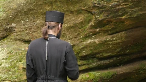 Clergy Crossing Himself in Front of Blessed Stone Monk in Black Clothing is Stock Footage 71631815