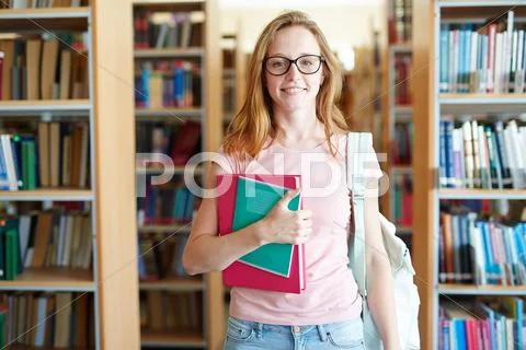 Clever girl with books and backpack in college library Stock Photos