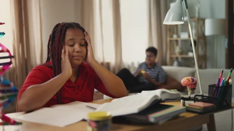 Clever girl doing homework while lazy brother plays video games on background Stock Footage 334947711