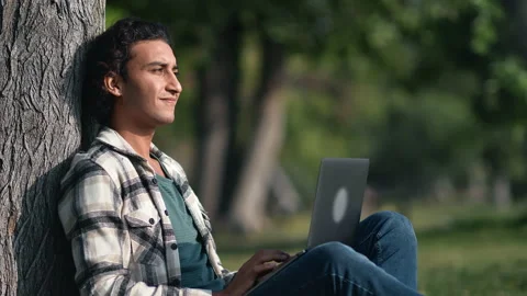 Clever modern mixed race guy working use laptop at summer sunny garden park Stock Footage 221013441