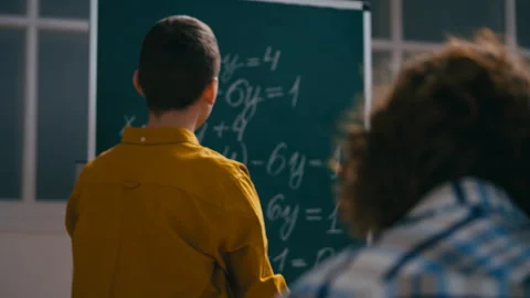 Clever teenage student explaining math equation solution near chalkboard, lesson Stock Footage 251805468