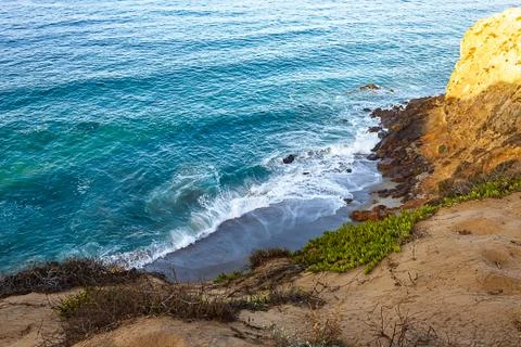 Clff side view of pacific ocean wavy shore and rocks, from sandy iceplant edged Stock Photos
