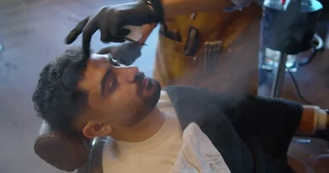 Client and barber reclining in chair, steadying forehead, shaping hairline with Stock Footage 337732022