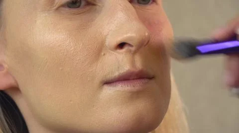 A client in a beauty salon does makeup. applies foundation to the face. Stock Photos
