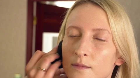 A client in a beauty salon does makeup. applies foundation to the face. Stock Photos