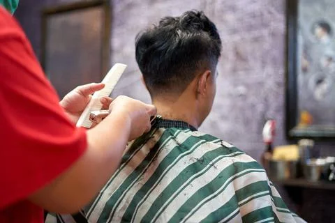 Client sitting on a chair while a barber shaving her nape Stock Photos
