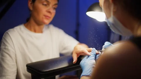 A client watches dust fly as gel polish is removed from her nails. Stock Footage 343528830