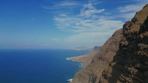 A cliff falling into the blue ocean, a wall of coastal cliffs with peaks. Stock Footage 266253304