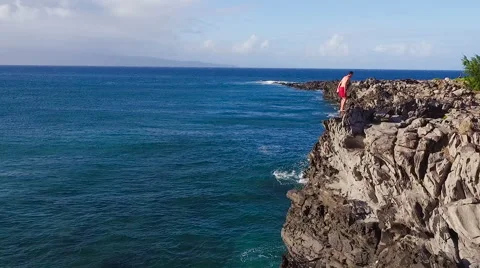 Cliff Jumping into Ocean. Aerial View Slow Motion. Young Man Jumps off Cliff  Stockbeeldmateriaal 57223006