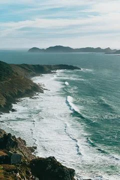 Cliff   side   view   of   wavy   ocean   and   large   hills Stock Photos