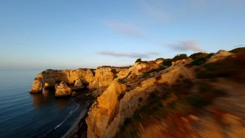 Cliffs bathed in golden sunset tones frame serene sea arches Video stock 346091472