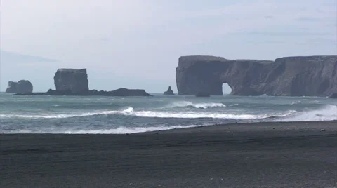 Cliffs with rock arch in the distance from black sand beach Stock Footage 37587044