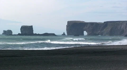 Cliffs in sea stack with rock arch in the distance from black sand beach Stock Footage 37588162