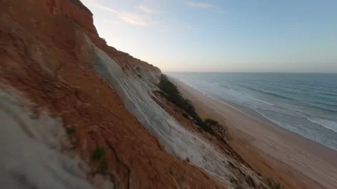 Cliffside coast with colorful strata, sandy beach, and ocean horizon Video stock 346090402