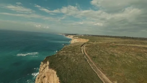 Cliffside road winds through grassy hills overlooking ocean waves Stock Footage 340226118