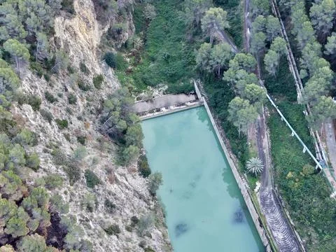 Cliffside water collection system adjacent to vibrant turquoise reservoir a.. Foto stock