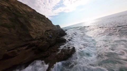Cliffside waves crash with power, sunlight reflects off sparkling blue water Stock Footage 340225572