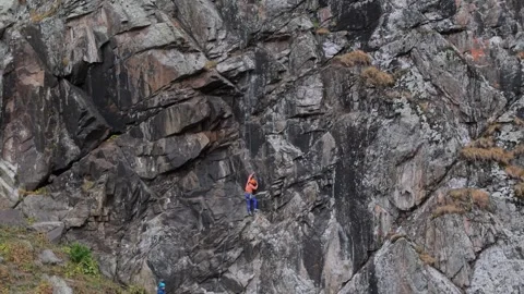 Climber ascends rocky cliff face with team supporting below in dynamic outdoor Video stock 316875715