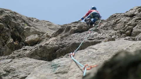 A climber ascends a rocky face under a clear sky, showcasing skill and 스톡 동영상 289541866