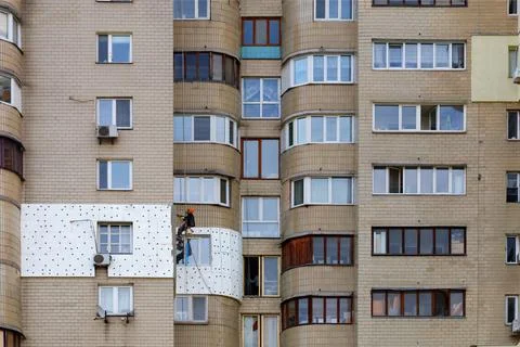 A climber builder on a suspended platform insulates the facade of a separate  Stock Photos