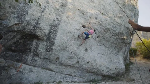 The climber climbs the rock, the boy-partner holds a safety rope Stock Footage 94590883