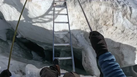 A climber crosses a large deep crack in the glacier by a metallic ladder Stock-Footage 208438164
