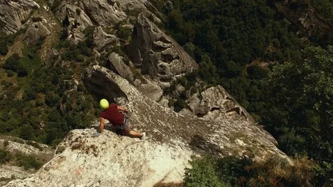 A climber is facing the edge of a cliff after he climbed. AERIAL Stock Footage 71890160