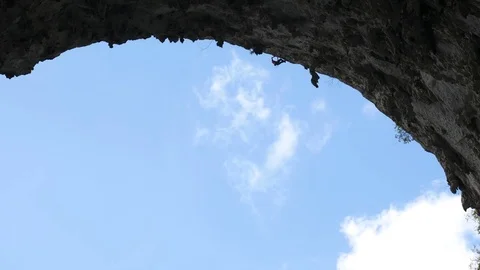 Climber in a Great Arch crag cave silhouetted against a blue summer sky Stock Footage 71390712