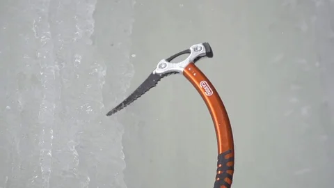 Climber hand breaking frozen ice with ice axe while climbing snowy cliff Stock Footage