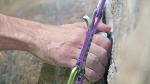 A climber secures gear while ascending a rocky cliff face on a sunny day in a Stock Footage 289543192