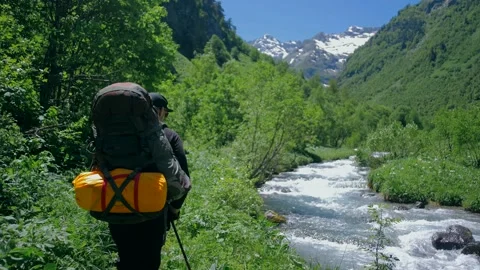 The climber walks along the path along the mountain river towards the high Stock Footage 138691017