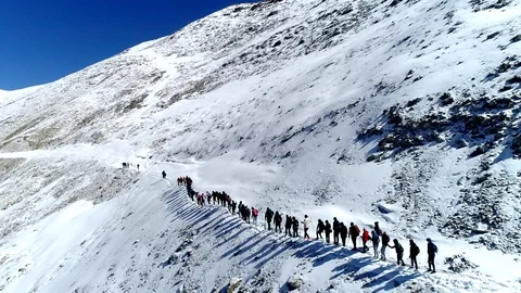 Climbers group in chain goes up snowy mountain slope to top. Drone aerial shot Stock Footage
